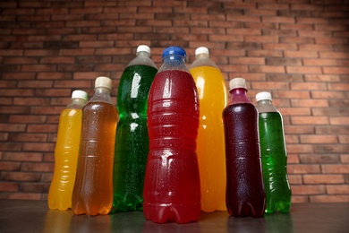 Bottles of soft drinks with water drops on table against brick wall, low angle view Photo of Bottles of soft drinks with water drops on table against brick wall, low angle view