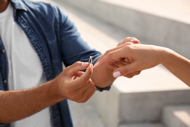 Man putting engagement ring on his girlfriend's finger outdoors, closeup Photo of Man putting engagement ring on his girlfriend's finger outdoors, closeup