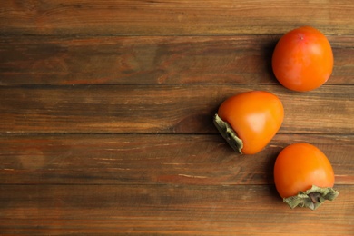 Tasty ripe persimmons on wooden table, flat lay. Space for text Photo of Tasty ripe persimmons on wooden table, flat lay. Space for text