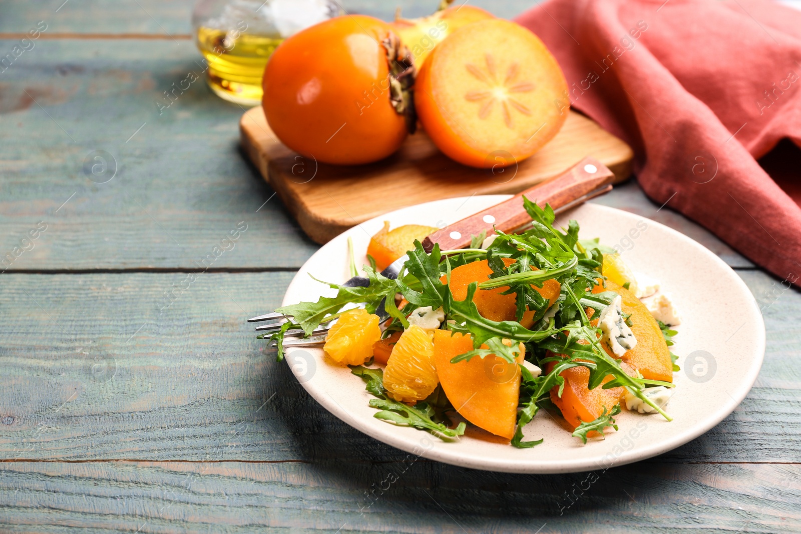 Delicious persimmon salad served on light blue wooden table Photo of Delicious persimmon salad served on light blue wooden table