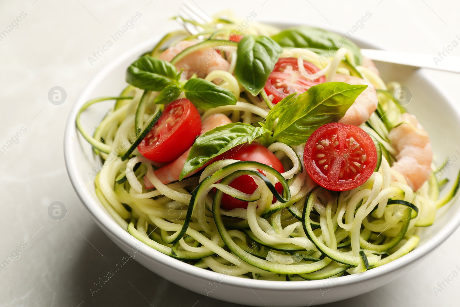 Delicious zucchini pasta with shrimps, cherry tomatoes and basil in bowl on light grey table, closeup Photo of Delicious zucchini pasta with shrimps, cherry tomatoes and basil in bowl on light grey table, closeup