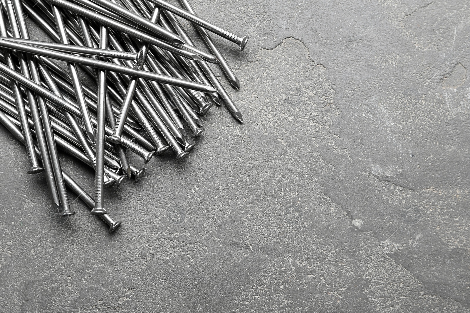 Pile of metal nails on grey stone background, flat lay. Space for text Photo of Pile of metal nails on grey stone background, flat lay. Space for text