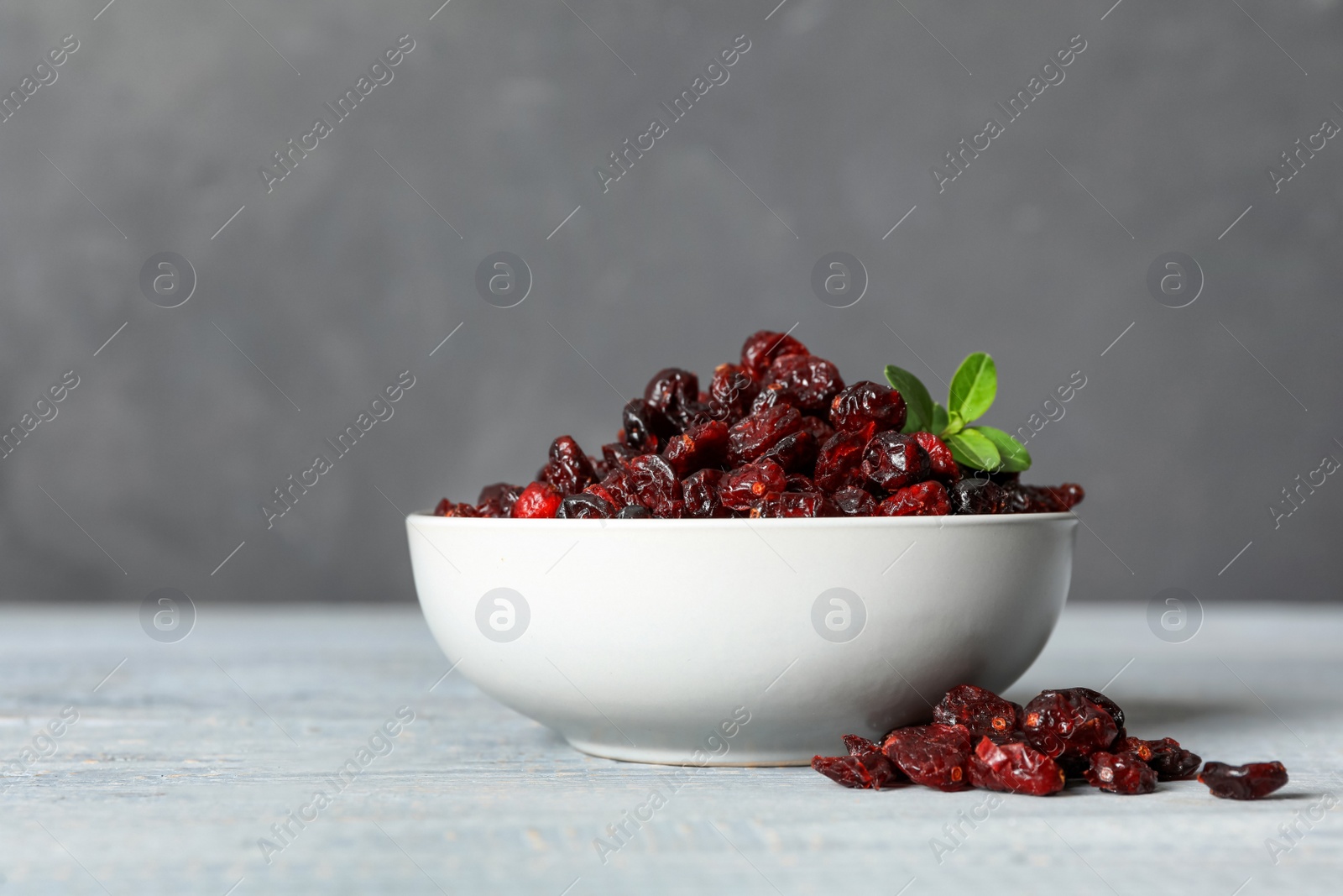 Tasty dried cranberries and leaves on wooden table against grey background Photo of Tasty dried cranberries and leaves on wooden table against grey background