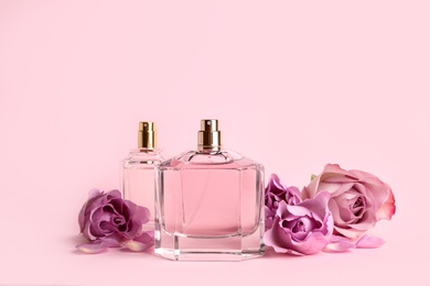 Bottles of perfume and beautiful roses on pink background Photo of Bottles of perfume and beautiful roses on pink background