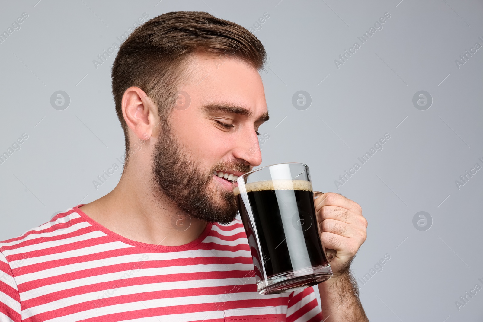 Handsome man with cold kvass on light grey background. Traditional Russian summer drink Photo of Handsome man with cold kvass on light grey background. Traditional Russian summer drink
