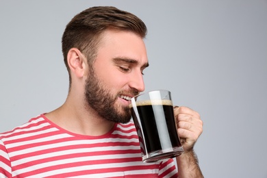 Handsome man with cold kvass on light grey background. Traditional Russian summer drink Photo of Handsome man with cold kvass on light grey background. Traditional Russian summer drink