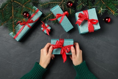 Woman holding Christmas gift box with red bow at dark grey table, top view Photo of Woman holding Christmas gift box with red bow at dark grey table, top view