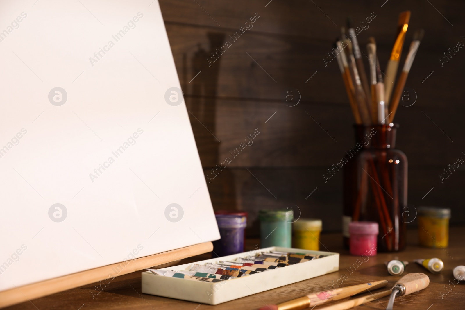 Easel with canvas and art supplies on wooden table Photo of Easel with canvas and art supplies on wooden table
