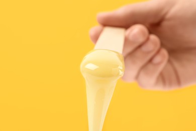 Woman holding spatula with hot depilatory wax on yellow background, closeup Photo of Woman holding spatula with hot depilatory wax on yellow background, closeup