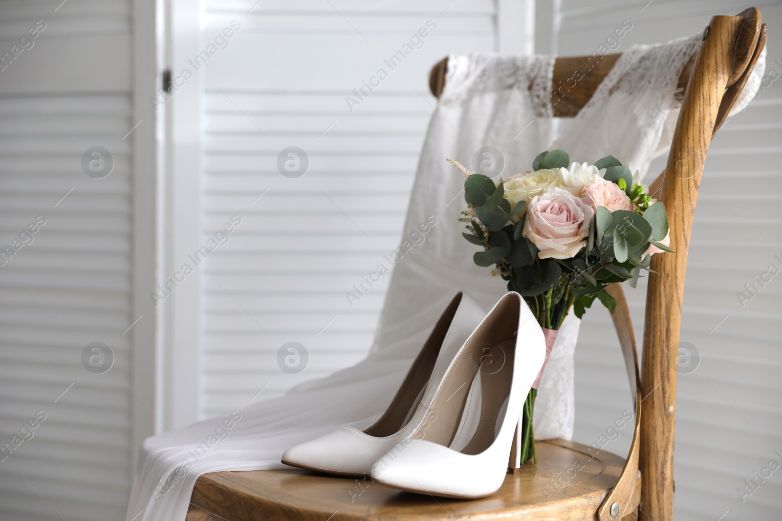 White high heel shoes, flowers and wedding dress on wooden chair indoors. Space for text Photo of White high heel shoes, flowers and wedding dress on wooden chair indoors. Space for text
