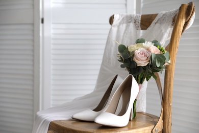 White high heel shoes, flowers and wedding dress on wooden chair indoors. Space for text Photo of White high heel shoes, flowers and wedding dress on wooden chair indoors. Space for text