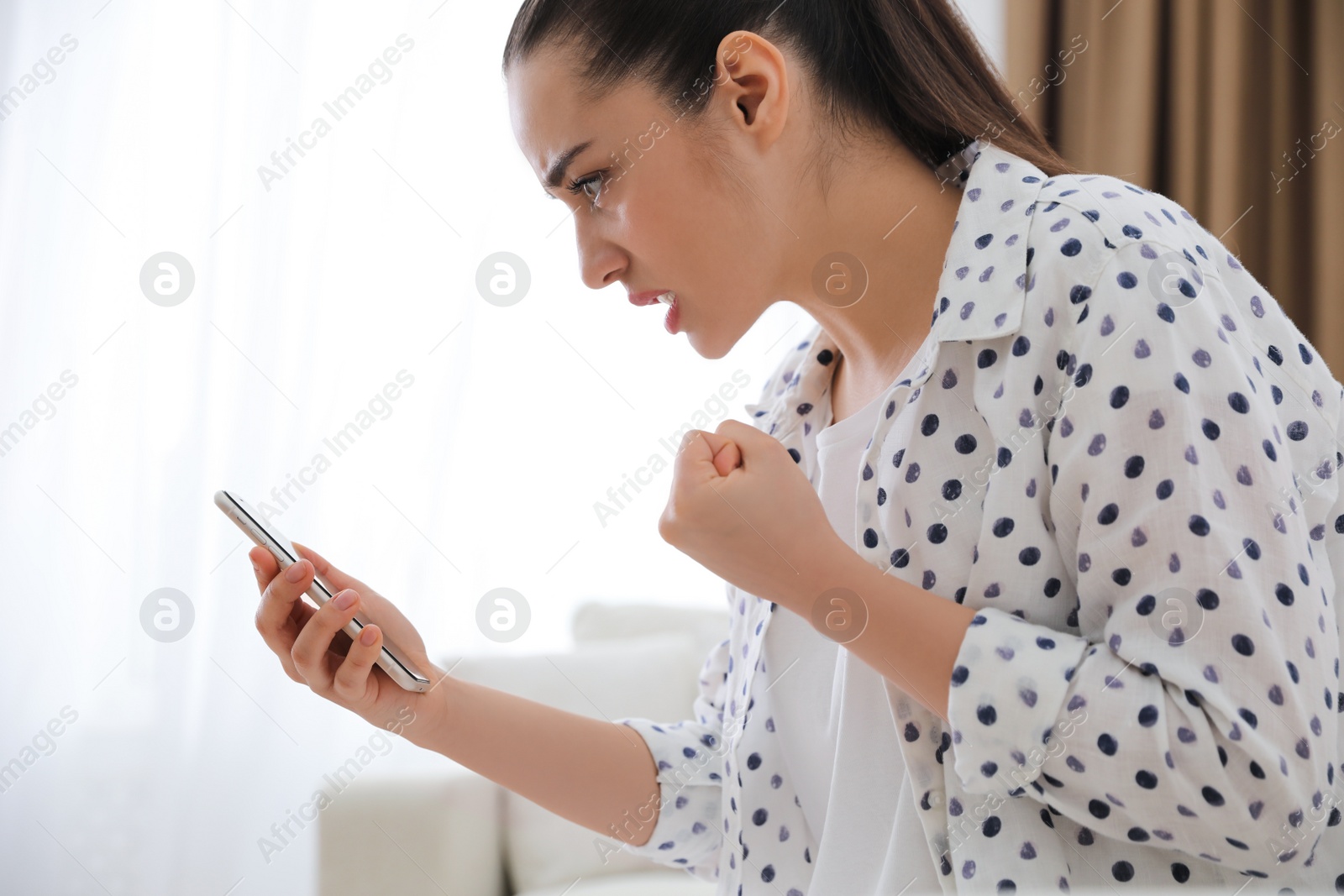 Emotional young woman with smartphone at home. Online hate concept Photo of Emotional young woman with smartphone at home. Online hate concept