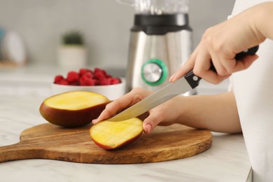 Woman preparing mango for tasty smoothie at white marble table in kitchen, closeup Photo of Woman preparing mango for tasty smoothie at white marble table in kitchen, closeup