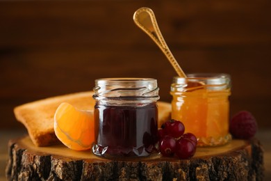 Jars with different sweet jams and ingredients on wooden stump Photo of Jars with different sweet jams and ingredients on wooden stump