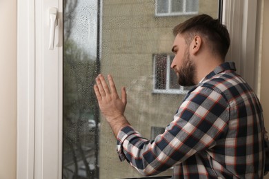 Depressed young man near window at home Photo of Depressed young man near window at home