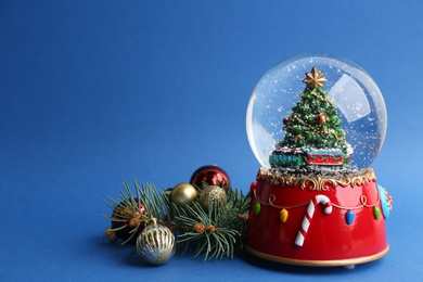 Beautiful snow globe, Christmas balls and fir branches on blue background, space for text Photo of Beautiful snow globe, Christmas balls and fir branches on blue background, space for text