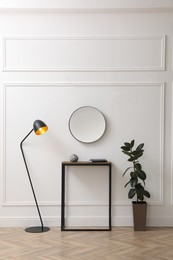 Console table, houseplant and lamp near light wall with mirror indoors. Interior design Photo of Console table, houseplant and lamp near light wall with mirror indoors. Interior design