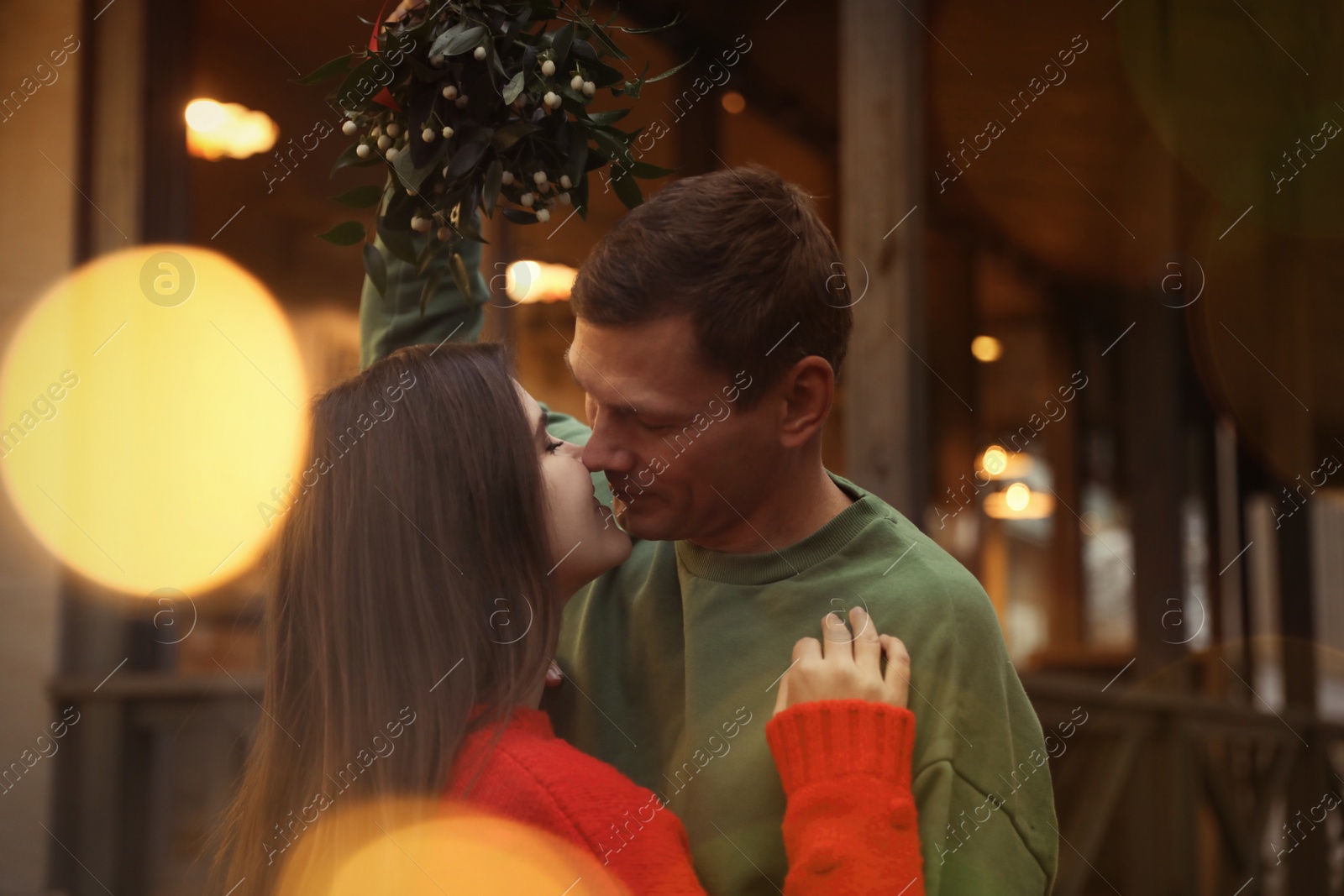 Happy couple kissing under mistletoe bunch outdoors, bokeh effect Photo of Happy couple kissing under mistletoe bunch outdoors, bokeh effect