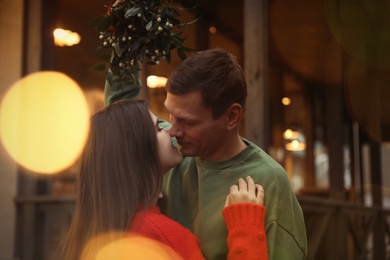 Happy couple kissing under mistletoe bunch outdoors, bokeh effect Photo of Happy couple kissing under mistletoe bunch outdoors, bokeh effect