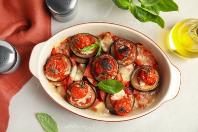 Baked eggplant with tomatoes, cheese and basil in dishware on light table, flat lay Photo of Baked eggplant with tomatoes, cheese and basil in dishware on light table, flat lay