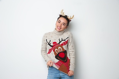 Young woman in Christmas sweater and deer headband on white background Photo of Young woman in Christmas sweater and deer headband on white background