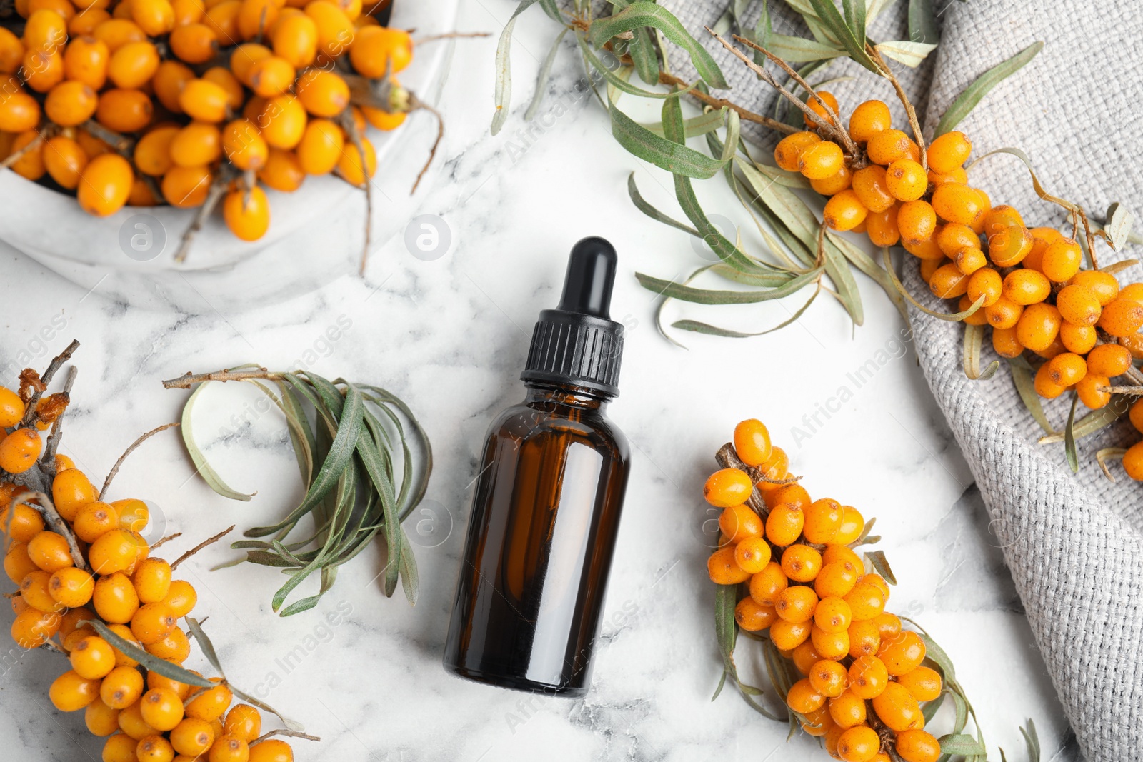 Natural sea buckthorn oil and fresh berries on white marble table, flat lay Photo of Natural sea buckthorn oil and fresh berries on white marble table, flat lay