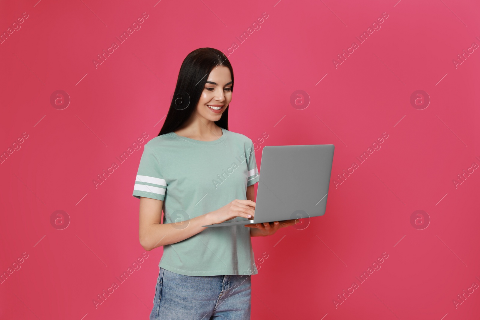 Young woman with modern laptop on pink background Photo of Young woman with modern laptop on pink background