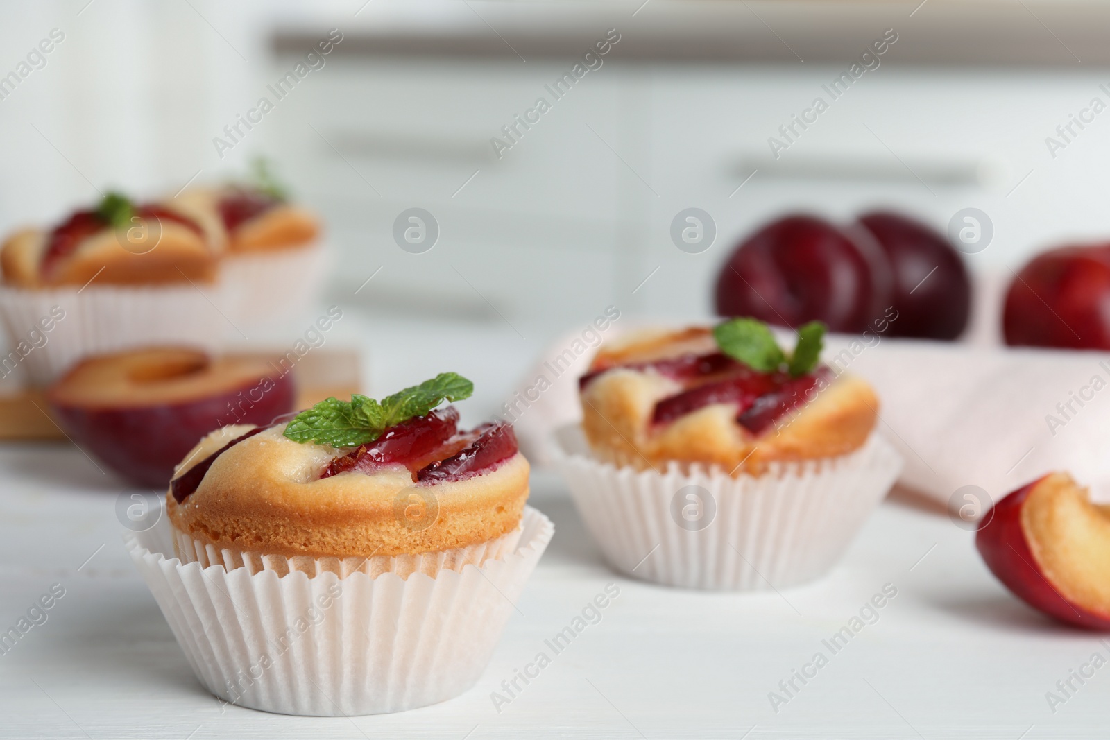 Delicious cupcakes with plums on white wooden table, closeup Photo of Delicious cupcakes with plums on white wooden table, closeup