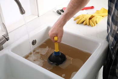 Man using plunger to unclog sink drain in kitchen, closeup Photo of Man using plunger to unclog sink drain in kitchen, closeup