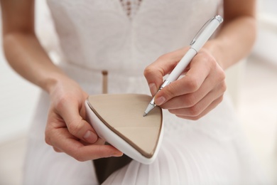 Young bride writing on her shoe indoors, closeup. Wedding superstition Photo of Young bride writing on her shoe indoors, closeup. Wedding superstition