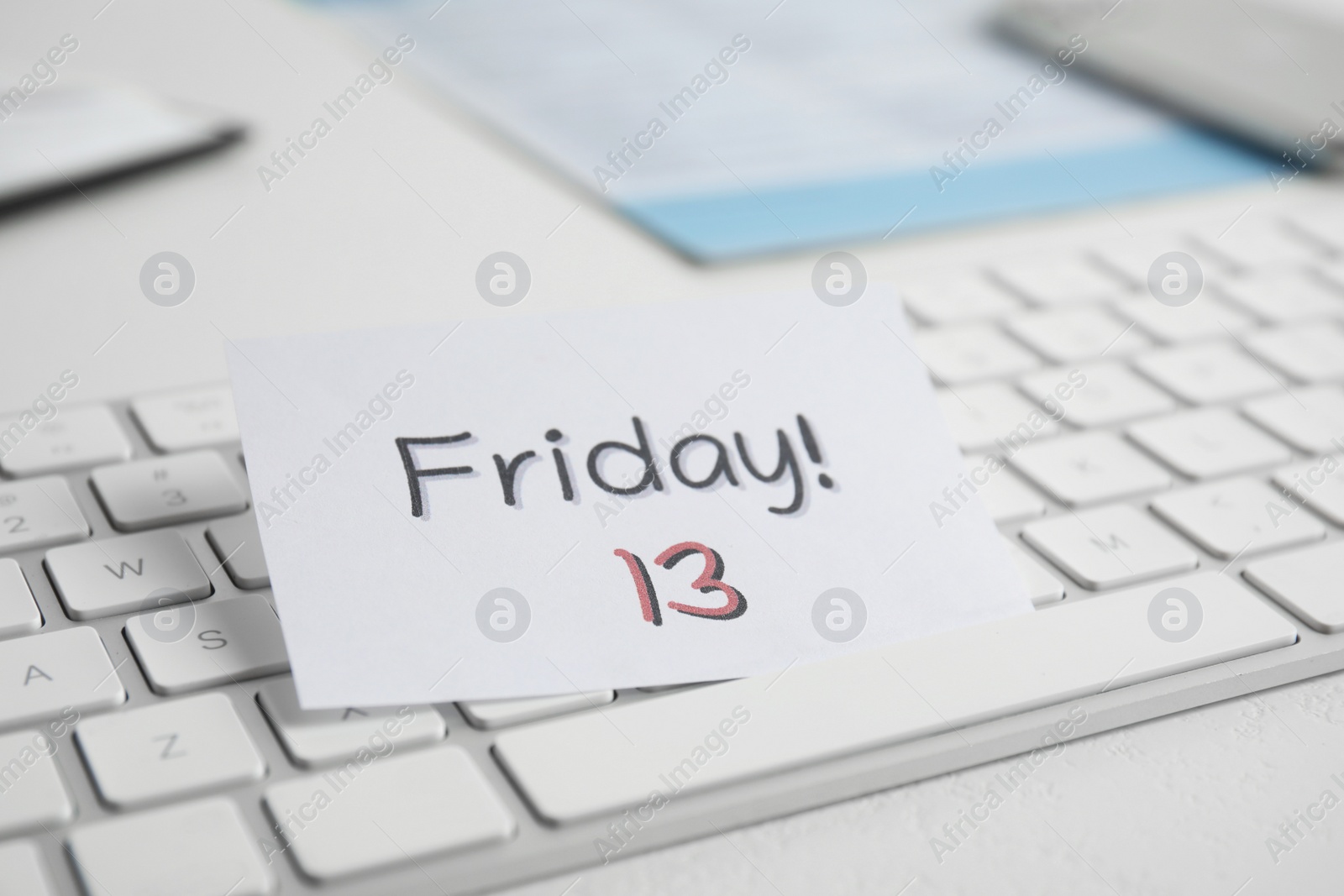Photo of Paper note with phrase Friday 13 and keyboard on white table. Superstition of bad luck