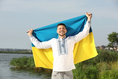 Man in vyshyvanka with flag of Ukraine outdoors Photo of Man in vyshyvanka with flag of Ukraine outdoors