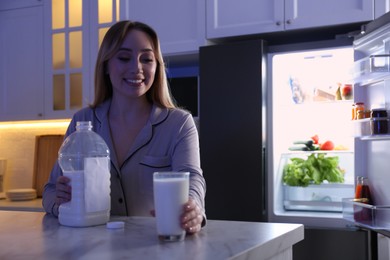 Young woman holding glass and gallon bottle of milk on white marble table in kitchen at night. Space for text Photo of Young woman holding glass and gallon bottle of milk on white marble table in kitchen at night. Space for text