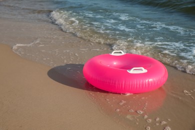Bright pink inflatable ring on sandy beach near sea Photo of Bright pink inflatable ring on sandy beach near sea