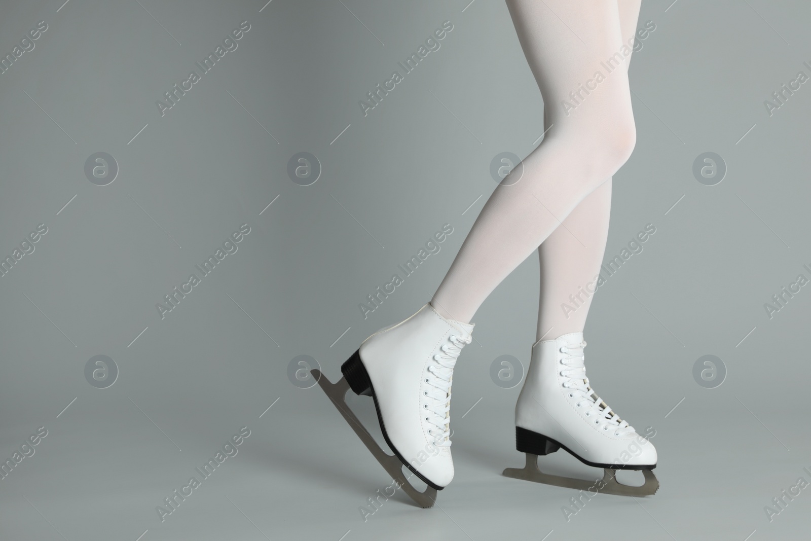 Woman in elegant white ice skates on grey background, closeup of legs. Space for text Photo of Woman in elegant white ice skates on grey background, closeup of legs. Space for text