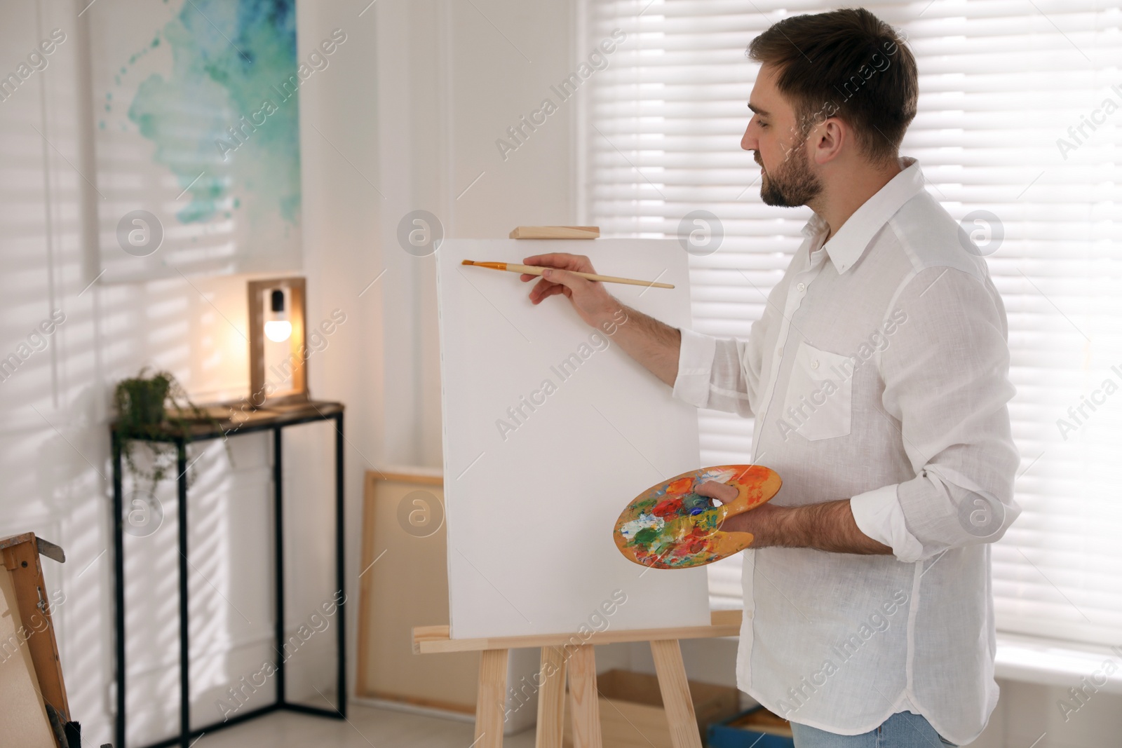 Young man painting on easel with brush in artist studio Photo of Young man painting on easel with brush in artist studio