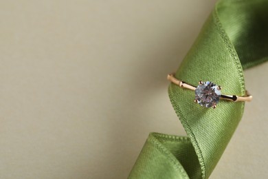 Beautiful engagement ring with gemstone on green ribbon against beige background, top view. Space for text Photo of Beautiful engagement ring with gemstone on green ribbon against beige background, top view. Space for text