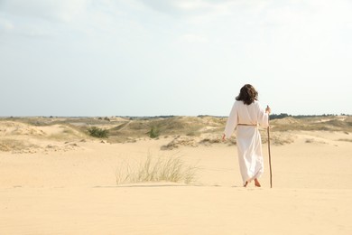 Jesus Christ walking with stick in desert, back view. Space for text Photo of Jesus Christ walking with stick in desert, back view. Space for text