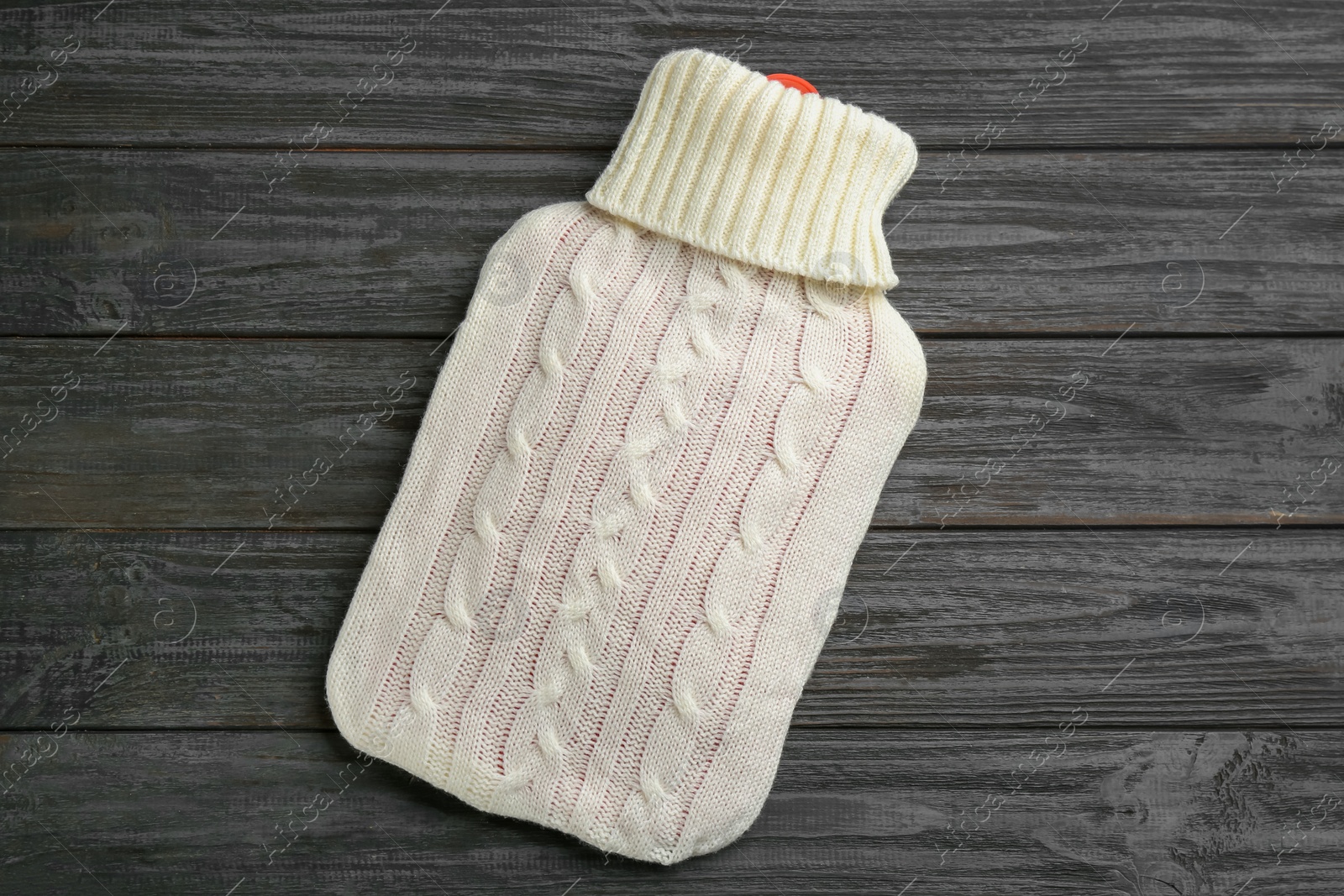 Hot water bottle with knitted cover on black wooden background, top view Photo of Hot water bottle with knitted cover on black wooden background, top view