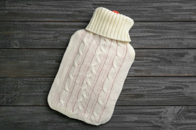 Hot water bottle with knitted cover on black wooden background, top view Photo of Hot water bottle with knitted cover on black wooden background, top view
