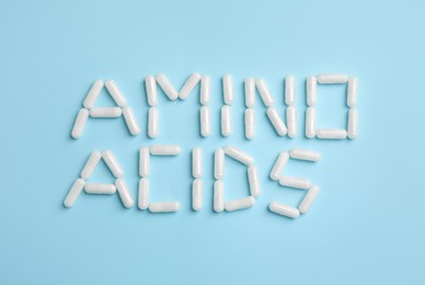 Phrase Amino acids made of pills on light blue background, flat lay Photo of Phrase Amino acids made of pills on light blue background, flat lay