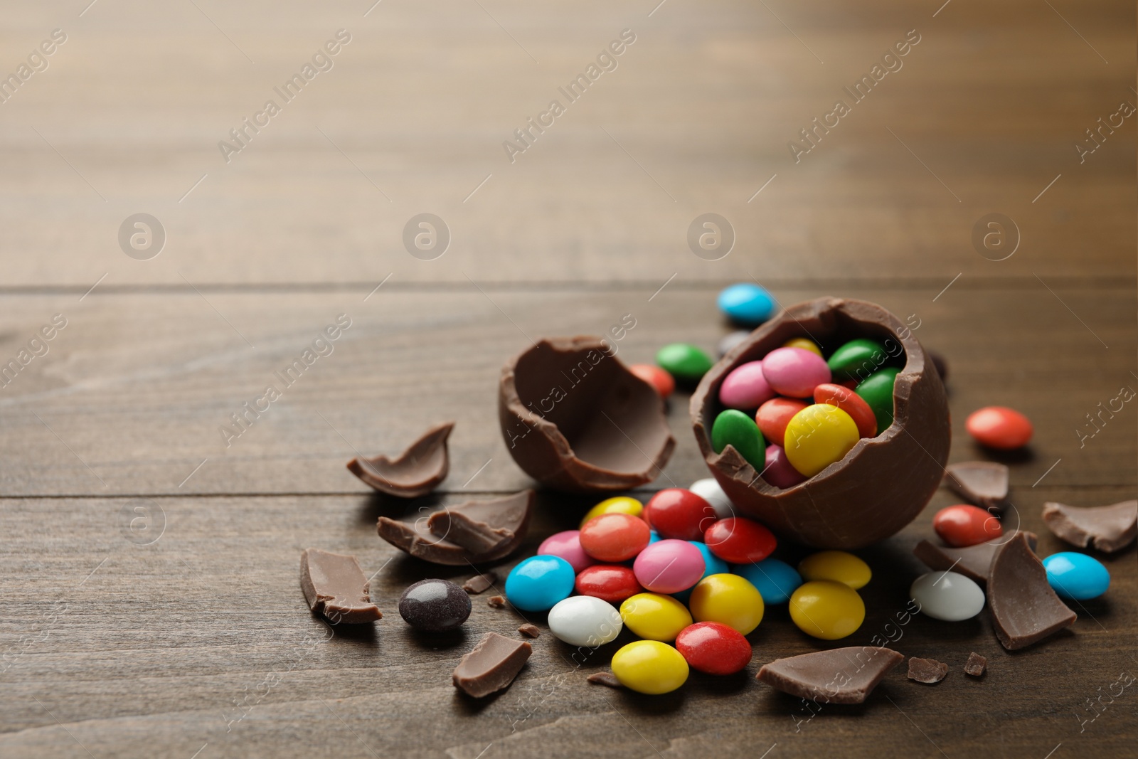 Broken chocolate egg and colorful candies on wooden table. Space for text Photo of Broken chocolate egg and colorful candies on wooden table. Space for text