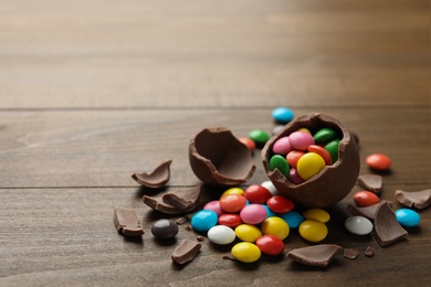 Broken chocolate egg and colorful candies on wooden table. Space for text Photo of Broken chocolate egg and colorful candies on wooden table. Space for text