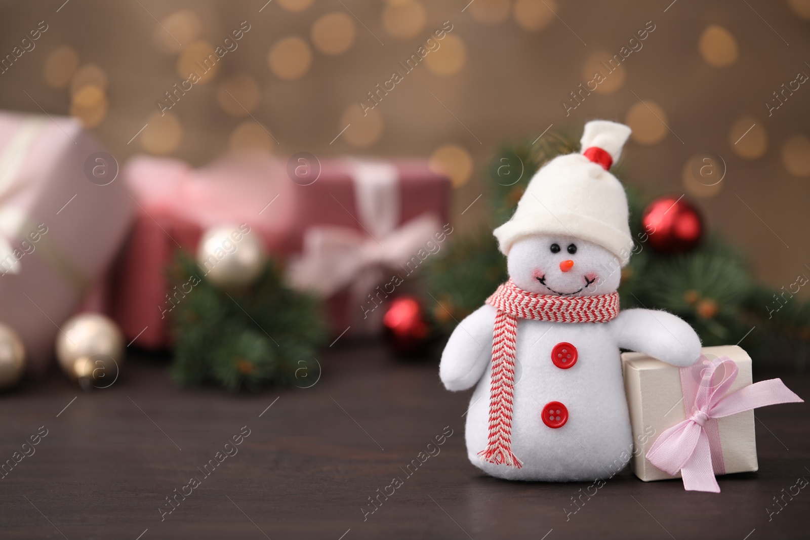 Photo of Snowman toy and Christmas box on table against blurred festive lights. Space for text
