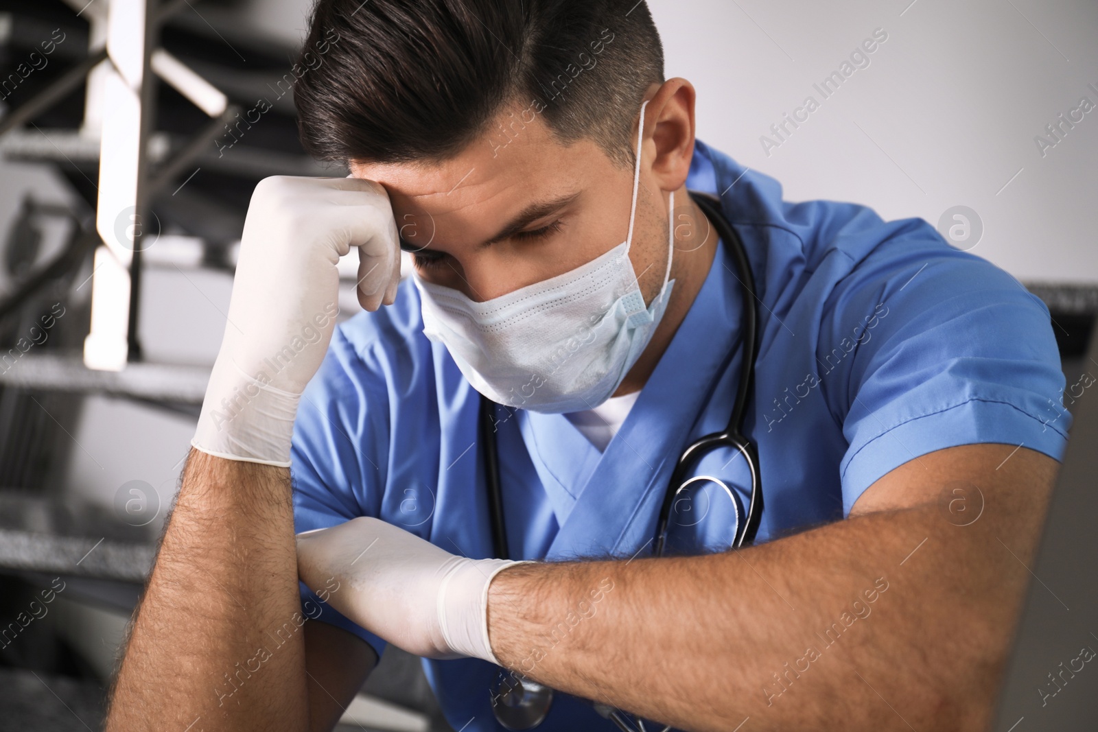 Sad doctor in facial mask on stairs indoors. Stress of health care workers during coronavirus pandemic Photo of Sad doctor in facial mask on stairs indoors. Stress of health care workers during coronavirus pandemic