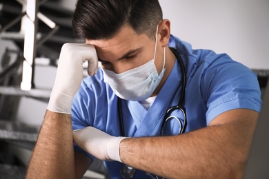 Sad doctor in facial mask on stairs indoors. Stress of health care workers during coronavirus pandemic Photo of Sad doctor in facial mask on stairs indoors. Stress of health care workers during coronavirus pandemic