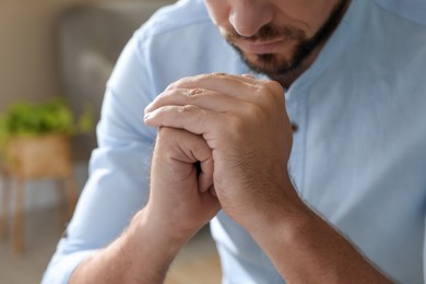 Religious man with clasped hands praying indoors, closeup Photo of Religious man with clasped hands praying indoors, closeup