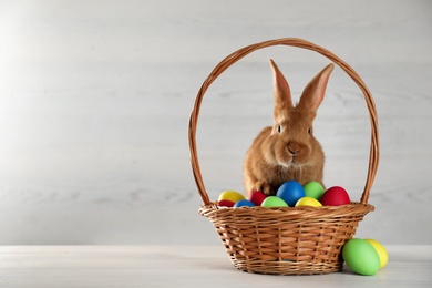 Cute bunny and basket with Easter eggs on white table. Space for text Photo of Cute bunny and basket with Easter eggs on white table. Space for text