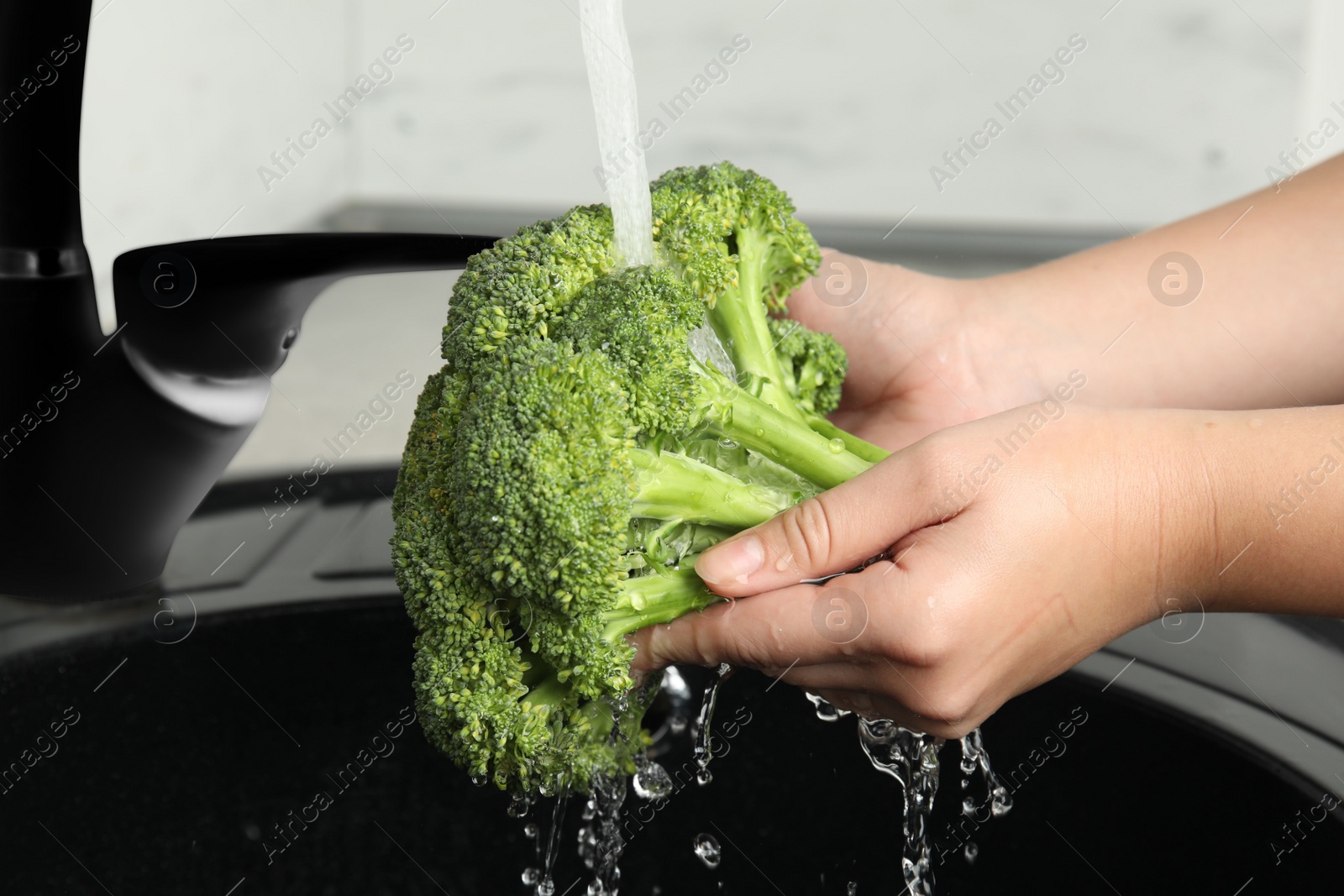 Woman washing fresh green broccoli in kitchen sink, closeup Photo of Woman washing fresh green broccoli in kitchen sink, closeup