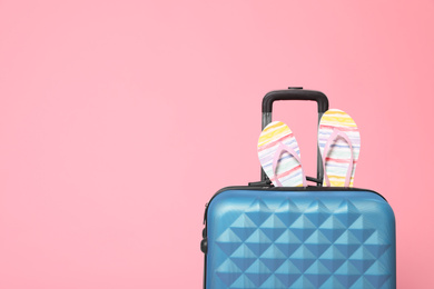 Photo of Stylish blue suitcase with flip flops on pink background. Space for text